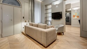 A modern living room with a sofa, a television, and a kitchen area in the background. - BDC - LuxuryLifeStyle (Roma)