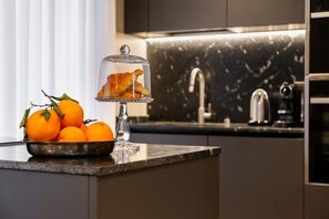 A kitchen counter with a bowl of oranges and a glass dome displaying croissants. - BDC - LuxuryLifeStyle (Roma)