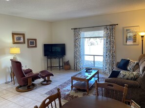 A living room with a TV, a sofa, a chair, a table, and a window with curtains.