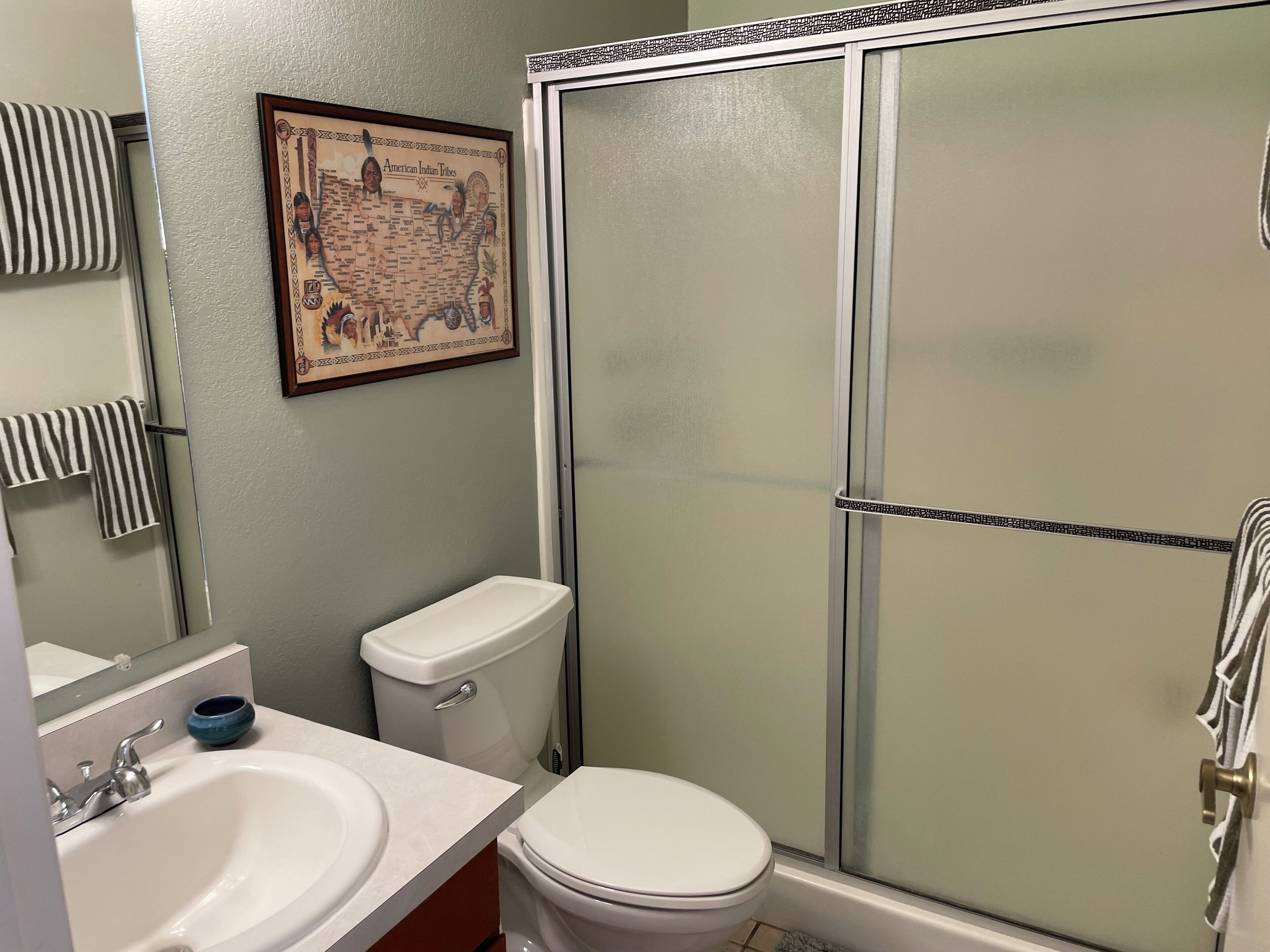A bathroom with a toilet, sink, and shower. There is a framed map on the wall.