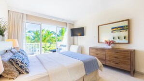 A bedroom with a large bed, a TV, a dresser, and a balcony with a view of palm trees. - Iberostate 2-Bedroom Condo - Terrace, BBQ, Beach Access, Lake & Golf Views (Punta Cana)