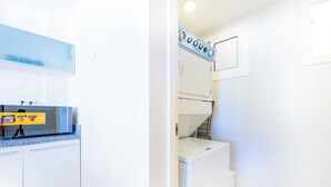 A compact kitchen with a microwave, a washing machine, and a small countertop. - Iberostate 2-Bedroom Condo - Terrace, BBQ, Beach Access, Lake & Golf Views (Punta Cana)