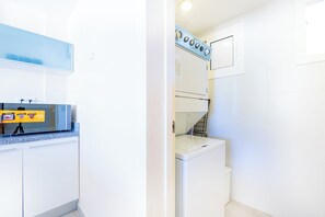 A compact kitchen with a microwave, a washing machine, and a small countertop. - Iberostate 2-Bedroom Condo - Terrace, BBQ, Beach Access, Lake & Golf Views (Punta Cana)