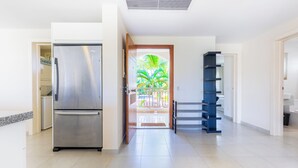 A modern kitchen with a stainless steel refrigerator, a wooden door leading to a balcony, and a blue shelving unit. - Iberostate 2-Bedroom Condo - Terrace, BBQ, Beach Access, Lake & Golf Views (Punta Cana)