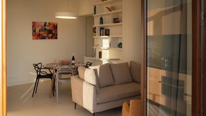 A modern living room with a sofa, dining table, chairs, and a bookshelf. - Residenza 2 Venti-Intera by Ortigia Apartments (Syracuse)
