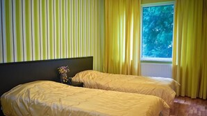 Une chambre avec deux lits, une table de chevet ornée d’un vase et une fenêtre avec des rideaux.