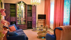 Un salon avec un canapé bleu, un fauteuil marron, un lustre, un téléviseur et une vitrine contenant des objets décoratifs.