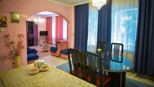 Un coin repas avec une table ronde, des chaises et un lustre. On aperçoit un canapé et un téléviseur à l’arrière-plan.