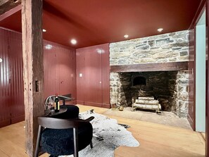 A room with a stone fireplace, wooden walls, and a rustic decor. - Classic Red Farmhouse Retreat by Nature Preserve (Patterson)