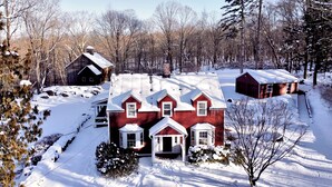 Ein rotes Haus mit schneebedecktem Dach, umgeben von einem Wald und einem klaren Himmel.