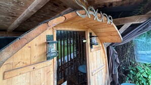 A wooden cabin with a curved entrance, a small table, and a chair outside. - Holiday Home Plattenstein with Private Terrace, Garden, Sauna, Wi-Fi and BBQ (Kirchberg im Wald)