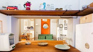 Et køkken med et træbord, en vintage-toaster, en grøn sofa og en væg med billeder.