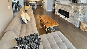 Een moderne woonkamer met een grote bank, een houten salontafel en een stenen openhaard.