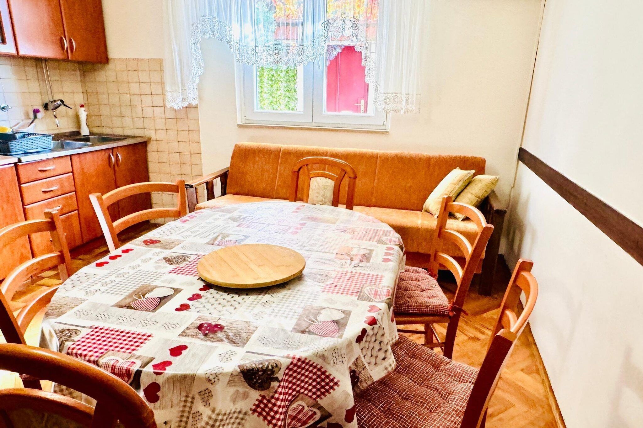 A dining area with a round table covered by a patchwork tablecloth, surrounded by wooden chairs.