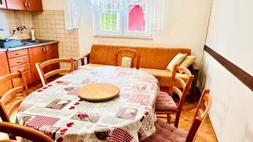 A dining area with a round table covered by a patchwork tablecloth, surrounded by wooden chairs.