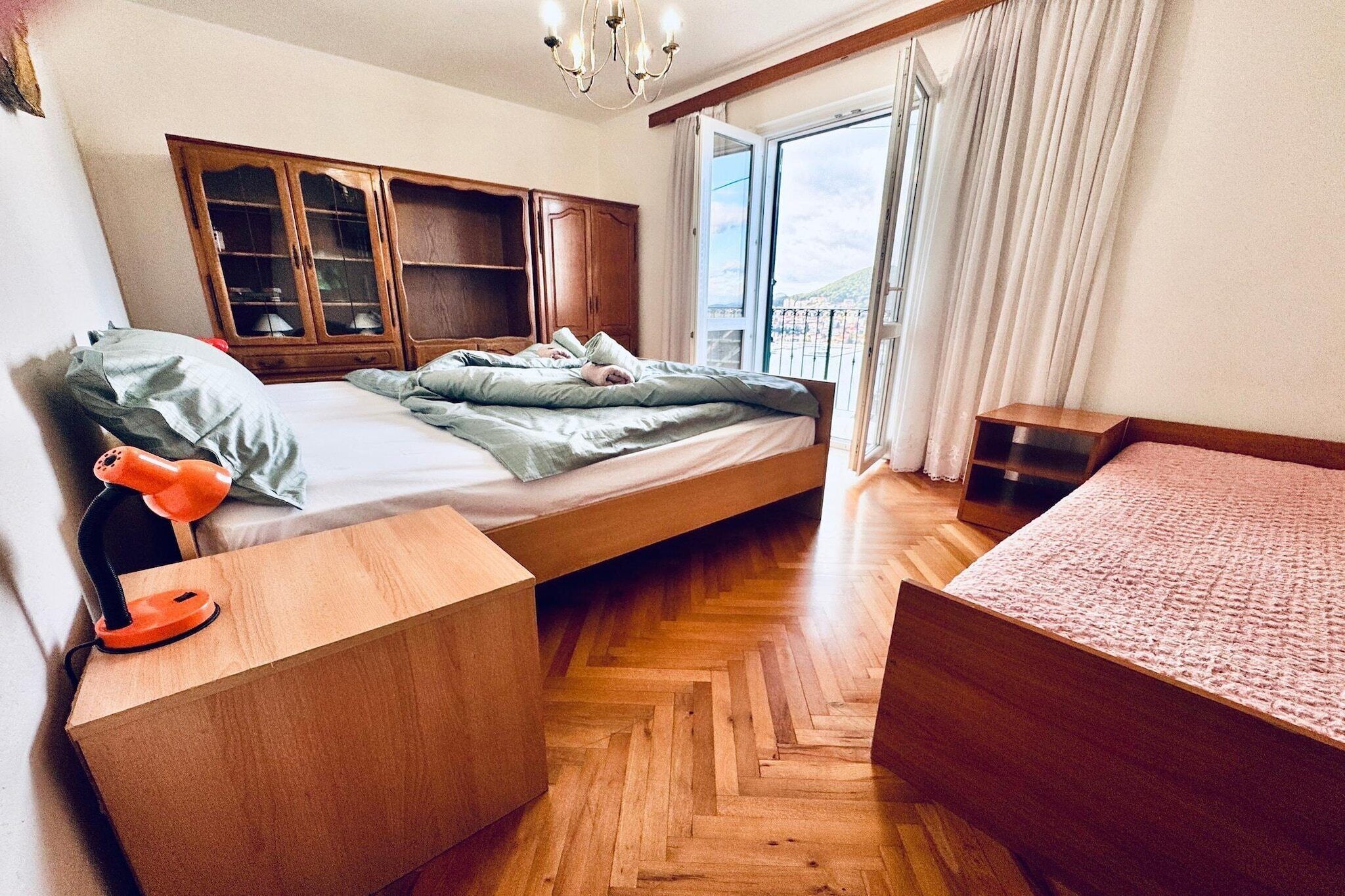 A bedroom with a bed, wooden wardrobe, bedside table, and a view of the outdoors.