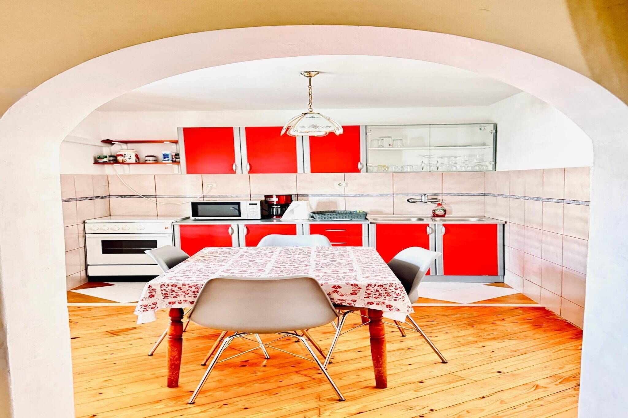 A compact kitchen with red cabinets, a white stove, and a dining table with chairs.