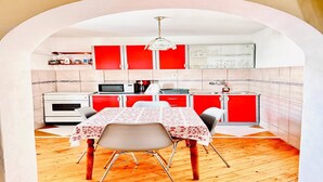 A compact kitchen with red cabinets, a white stove, and a dining table with chairs. - Spacious Stone Villa with Sea Views (Dubrovnik)