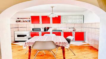 A compact kitchen with red cabinets, a white stove, and a dining table with chairs.