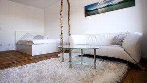 A modern bedroom with a glass coffee table, a white sofa, and a painting of a landscape.