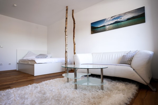 Une chambre à coucher moderne avec une table basse en verre, un canapé blanc et un tableau représentant un paysage.