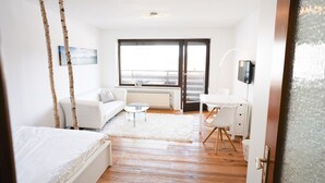 A modern hotel room with a bed, a sofa, a desk, and a large window.