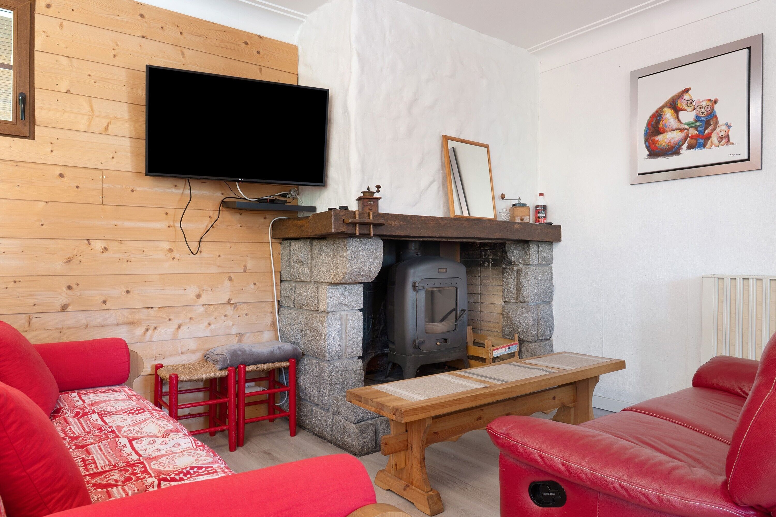 Un salon chaleureux avec une cheminée en pierre, un canapé en cuir rouge, une table en bois et un téléviseur à écran plat fixé au mur.