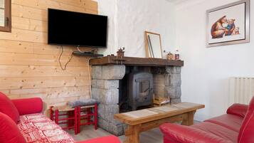 Un salon chaleureux avec une cheminée en pierre, un canapé en cuir rouge, une table en bois et un téléviseur à écran plat fixé au mur.