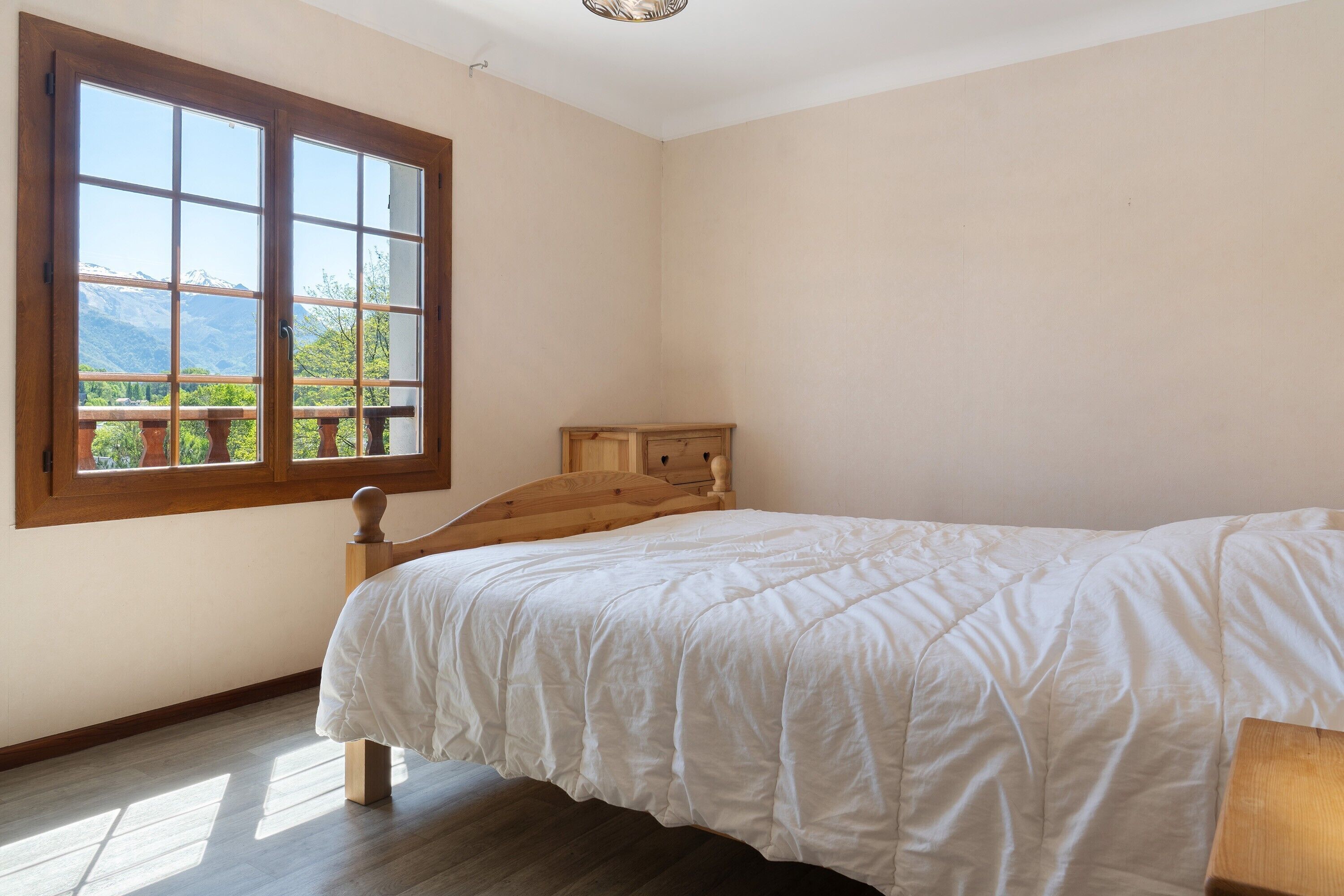 A bedroom with a wooden bed, a large window with a view of mountains, and a wooden headboard.