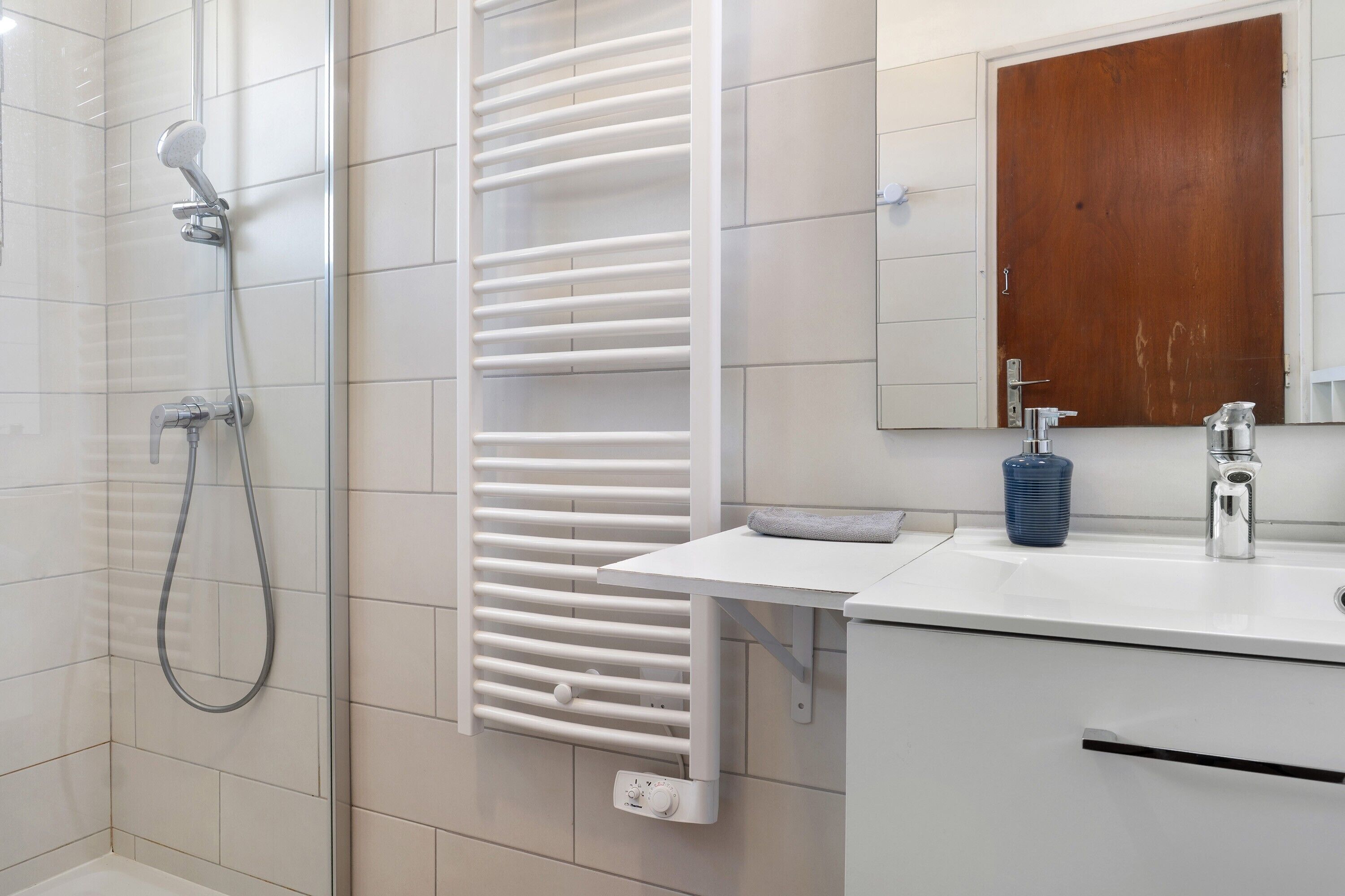 Een moderne badkamer met een douche, een witte handdoekhouder, een wastafel met spiegel en een houten deur.