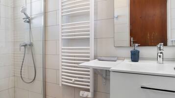 Een moderne badkamer met een douche, een witte handdoekhouder, een wastafel met spiegel en een houten deur.