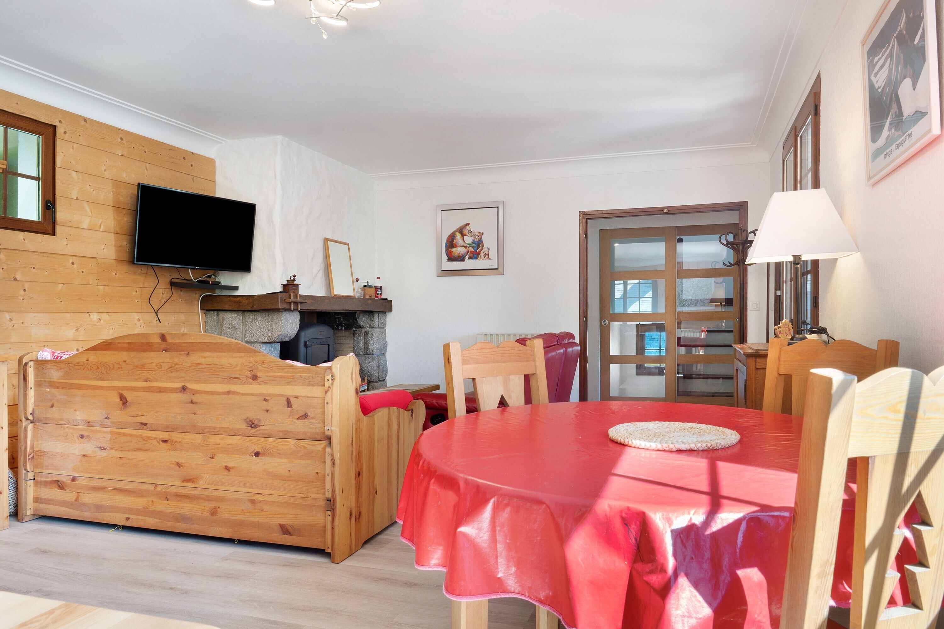 Ein gemütliches Zimmer mit einem hölzernen Bett, einem roten Tisch und einem Fernseher an der Wand.