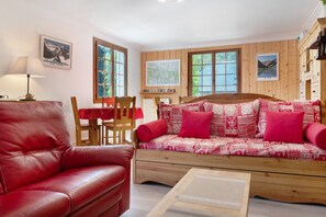 Een gezellige kamer met een rode leren bank, houten wanden, een houten bed met beddengoed met patroon en een tafel met stoelen.