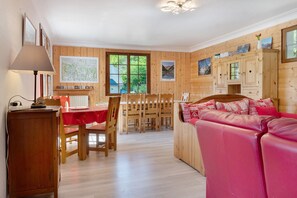 Een kamer met houten lambrisering, een eettafel, stoelen, een rode bank en een kast.