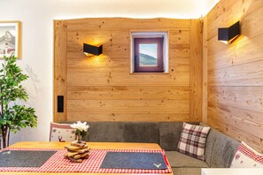 A cozy room with a wooden wall, a sofa, a table with a checkered table runner, and a framed picture. - Ammerstube – Alpine Design Holiday Apartment in Central Oberammergau (Oberammergau)