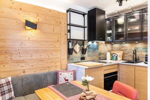 A kitchen with wooden walls, a built-in oven, a sink, and a dining area with a table and chairs.