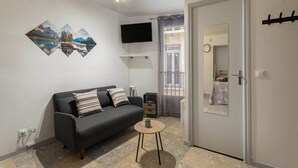 Ein modernes Wohnzimmer mit einer Couch, einem kleinen Tisch, einem an der Wand befestigten Fernseher und einer Tür zum Balkon.