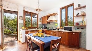 A kitchen with wooden cabinets, a dining table with chairs, a microwave, and a window with a view of greenery. - Il giardino dei Gigli, few steps from the sea (Meta)