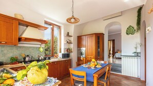 A kitchen with wooden cabinets, a dining table with chairs, a hanging light fixture, and a view of the dining area. - Il giardino dei Gigli, few steps from the sea (Meta)