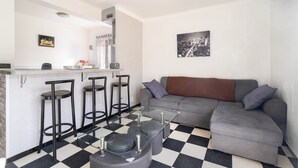 A modern living area with a sofa, a glass coffee table, and a kitchen area with a bar stool.