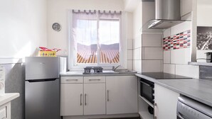 A modern kitchen with a stainless steel refrigerator, a microwave, and a dishwasher. There is a window with a view of a tiled roof.