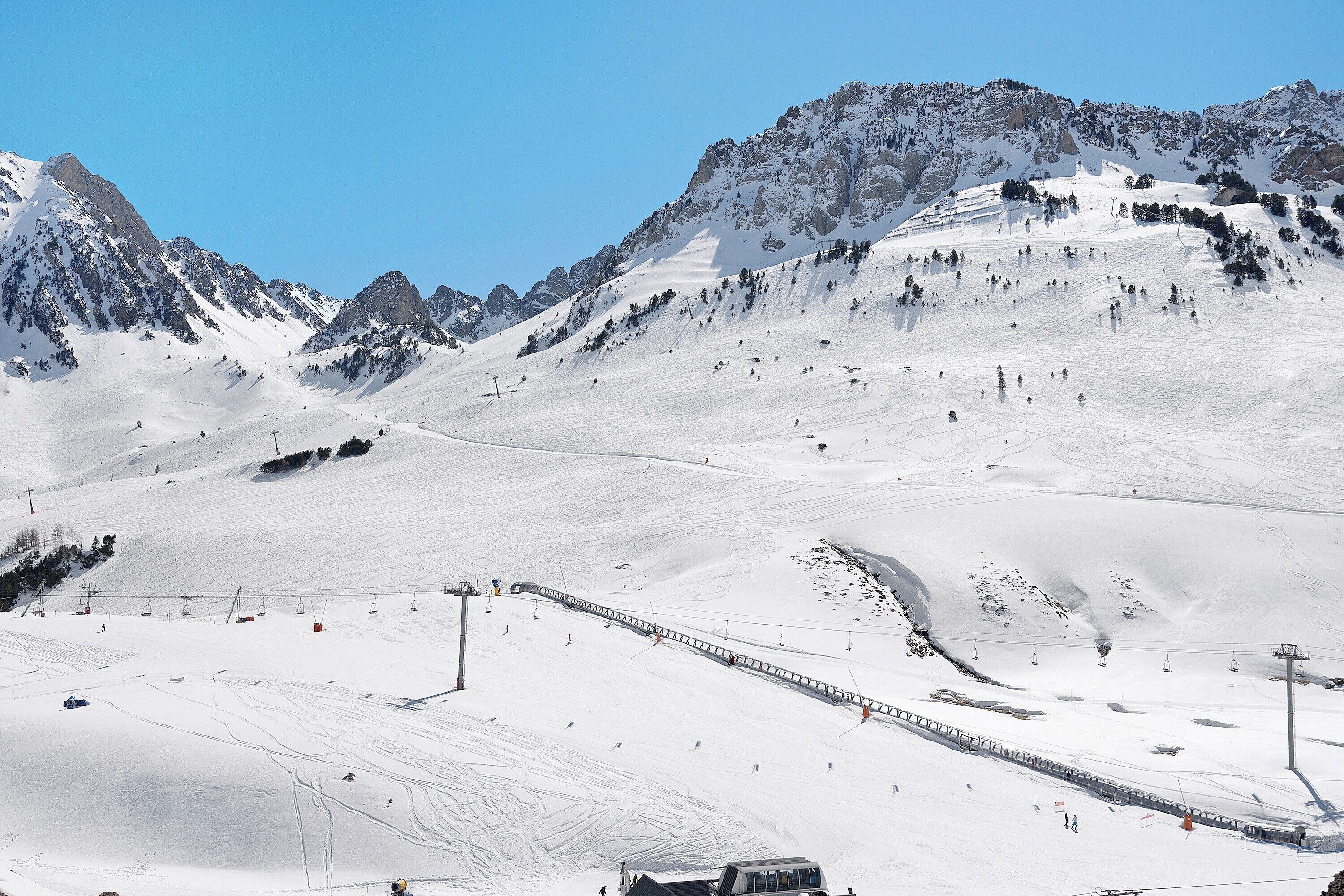Eine verschneite Berglandschaft mit Skipisten, einer Seilbahn und blauem Himmel.