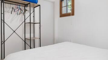 Une chambre à coucher avec un lit, une armoire où sont rangés des vêtements, et une fenêtre donnant sur un beau paysage.