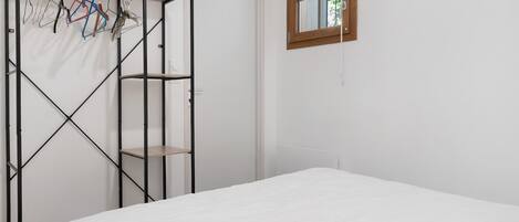 A bedroom with a bed, a wardrobe with hanging clothes, and a window with a view.