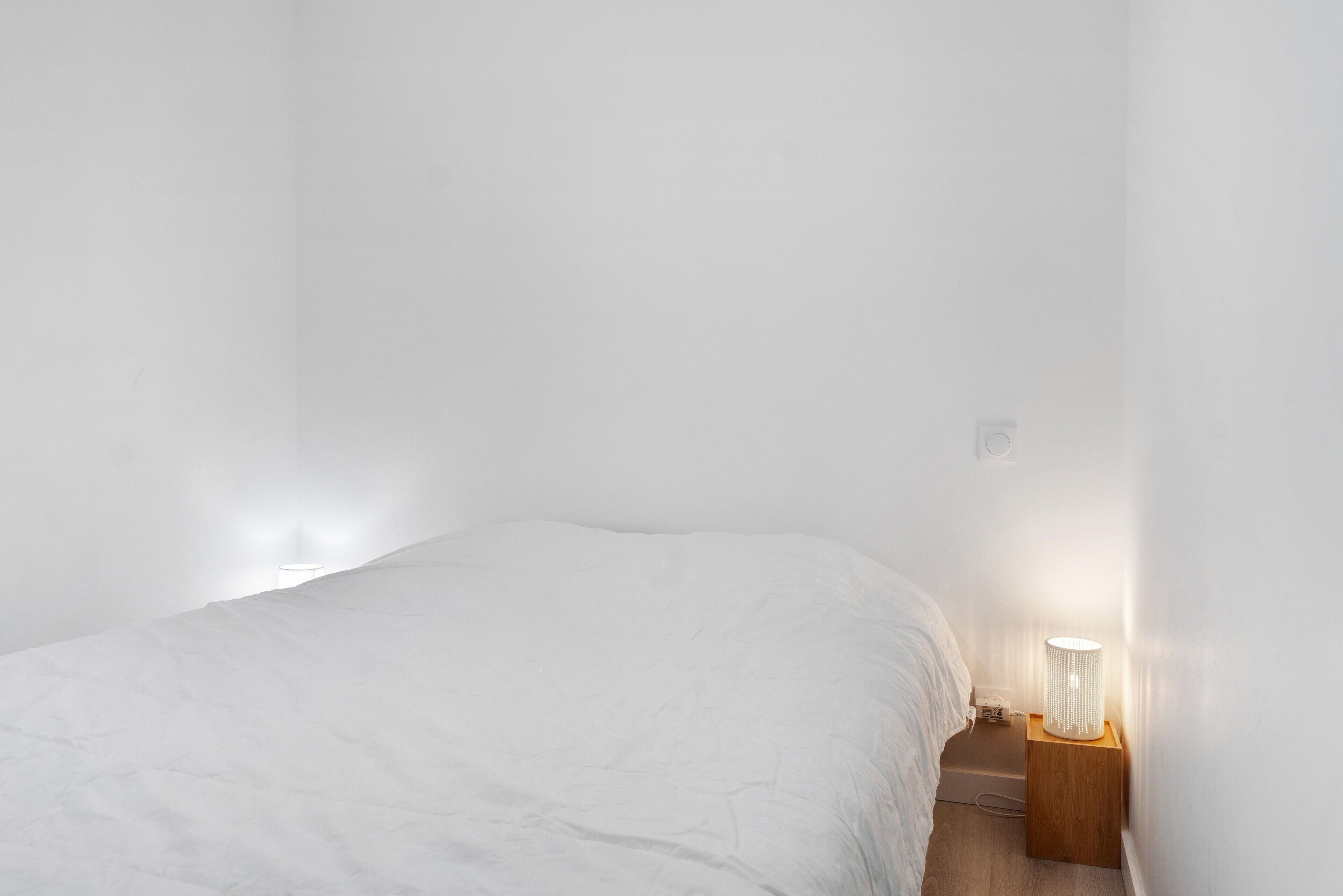 A bedroom with a bed, a nightstand, and a wall-mounted lamp.