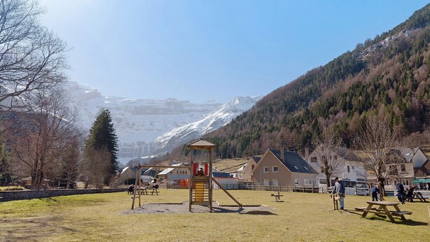 A playground with a slide and climbing structure, picnic tables, and houses in the background. - Apartment 'L'arrieulat 2' with Mountain View, Shared Terrace and Shared Garden (Argelès-Gazost)