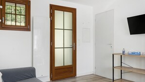 A room with a wooden door, a white wall, a grey sofa, and a wooden shelf with items. - Apartment 'L'arrieulat 2' with Mountain View, Shared Terrace and Shared Garden (Argelès-Gazost)