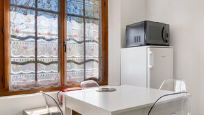 A room with a white table, a microwave, a refrigerator, and a window with a floral curtain. - Apartment 'L'arrieulat 2' with Mountain View, Shared Terrace and Shared Garden (Argelès-Gazost)