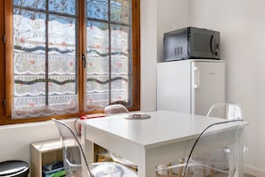 Een kamer met een witte tafel, een magnetron, een koelkast en een raam met een bloemenprint gordijn.