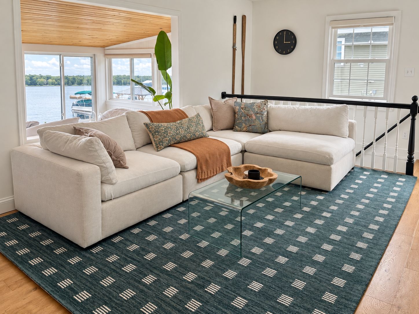 A living room with a sectional sofa, a glass coffee table, and a view of a lake.